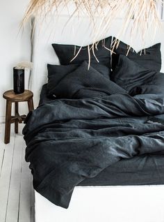 a bed with black linens and pillows on top of it next to a side table