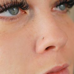 a close up of a woman's face with long lashes and piercing on her nose