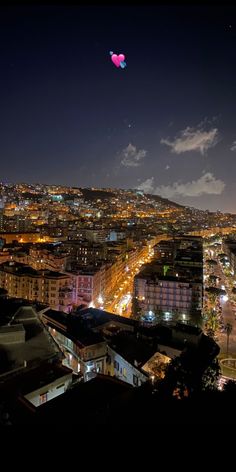 a view of a city at night from the top of a hill with a kite flying in the sky