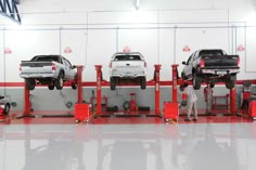 two men working on three cars in a car repair shop with red and white lines