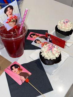 two cupcakes on a table next to a drink and some cards with photos