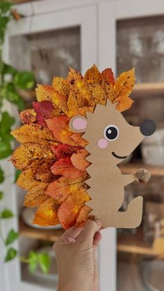 a hand holding up a paper hedge with autumn leaves on it's head and eyes