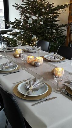 a dining room table set with place settings and christmas tree in the backround