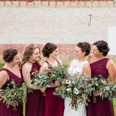 a group of women standing next to each other in front of a brick wall holding bouquets