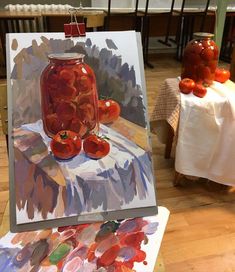 an easel with a painting on top of it and some tomatoes in the background