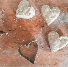 four heart shaped cookie cutters sitting on top of a wooden table covered in powdered sugar