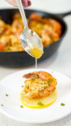 a person is pouring sauce on a plate with shrimp and lemons in the background