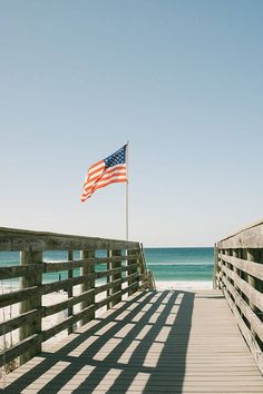 an american flag is flying on the pier by the beach in front of the ocean