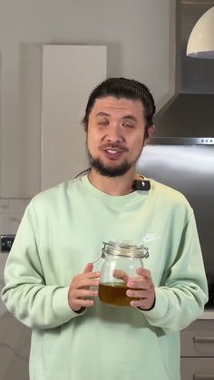 a man holding a jar with liquid in it and making a funny face while standing in front of a refrigerator