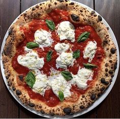 a pizza topped with mozzarella and basil on a white plate sitting on a wooden table