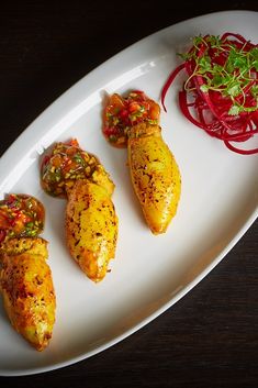 four pieces of chicken on a white platter with a side of red onions and green sprouts