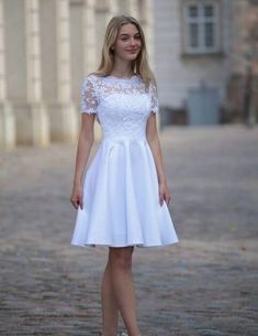 a woman standing in front of a building wearing a white dress and high heel shoes