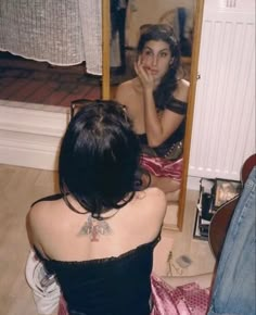 a woman sitting in front of a mirror looking at her own reflection on the floor