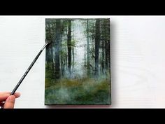 a person holding a paintbrush in front of a painting on a canvas with trees and grass