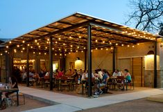 a group of people sitting at tables under a covered area with lights on the roof