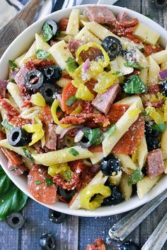 pasta salad with olives, tomatoes, and ham in a white bowl on a wooden table