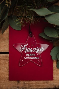 a red christmas ornament hanging from a tree with greenery around it on a wooden surface