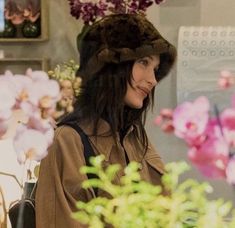 a woman wearing a brown coat and hat in front of pink flowers on display at a flower shop