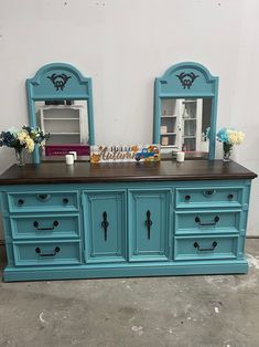 a blue dresser with two mirrors and vases on top