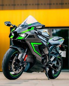 a green and black motorcycle parked in front of a yellow building with its lights on