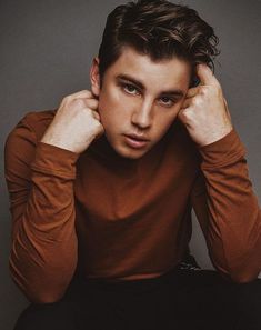 a young man sitting down with his hands on his head and looking at the camera