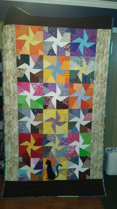 a cat sitting in front of a colorful quilt