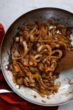 onions being cooked in a pan with a wooden spoon