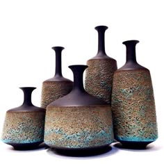 four vases are sitting in a row on the floor, one has blue and brown speckles