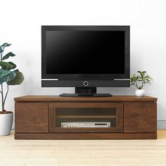 a flat screen tv sitting on top of a wooden entertainment center next to a potted plant