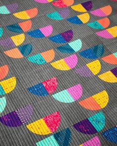 a colorful quilt is laying on top of a gray tablecloth with multicolored circles