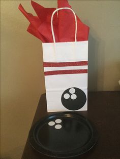 a paper bag sitting on top of a table next to a black plate with a bowling ball painted on it