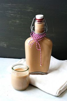 a bottle of liquid next to a glass jar with a pink ribbon tied around it