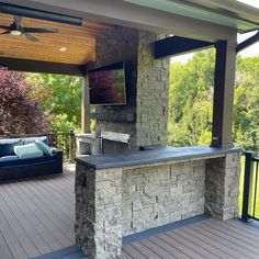 an outdoor living area with stone fireplace and tv on the back wall, surrounded by wooden decking