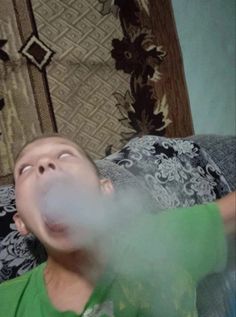 a young boy laying on top of a couch next to a stuffed animal and blowing bubbles