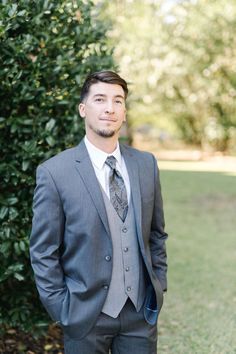 a man in a suit and tie standing next to a bush with his hands in his pockets