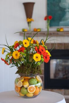 a vase filled with flowers and fruit on top of a table next to a fireplace