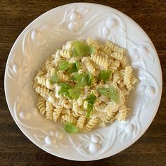 a white plate topped with pasta covered in sauce and garnished with green leaves