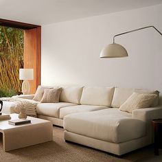 a living room with white couches and pillows on the floor next to a large window