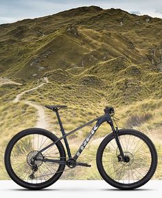 a mountain bike parked on the side of a road in front of a grassy hill