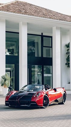 a red and black sports car parked in front of a white building with columns on the side