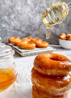 honey being drizzled over glazed doughnuts on a white tablecloth