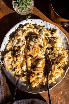 a white plate topped with pasta covered in cheese and mushrooms next to a glass of wine