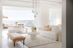 a living room filled with white furniture next to an ocean side house entrance area and balcony