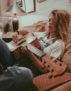 a woman sitting on a couch playing an acoustic guitar