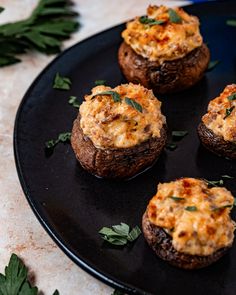 four stuffed mushrooms with cheese and herbs on a black plate