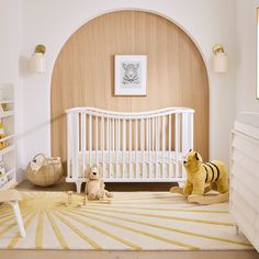 a baby's room with a white crib, yellow rug and stuffed animals