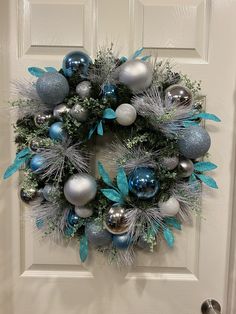 a wreath with silver and blue ornaments hanging on the front door