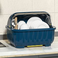 a blue container filled with white dishes on top of a counter next to a clock