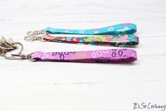 three keychains with different designs on them sitting on a white wooden surface,