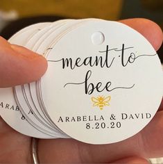 a person holding four small round tags with the words meant to bee on them in black ink